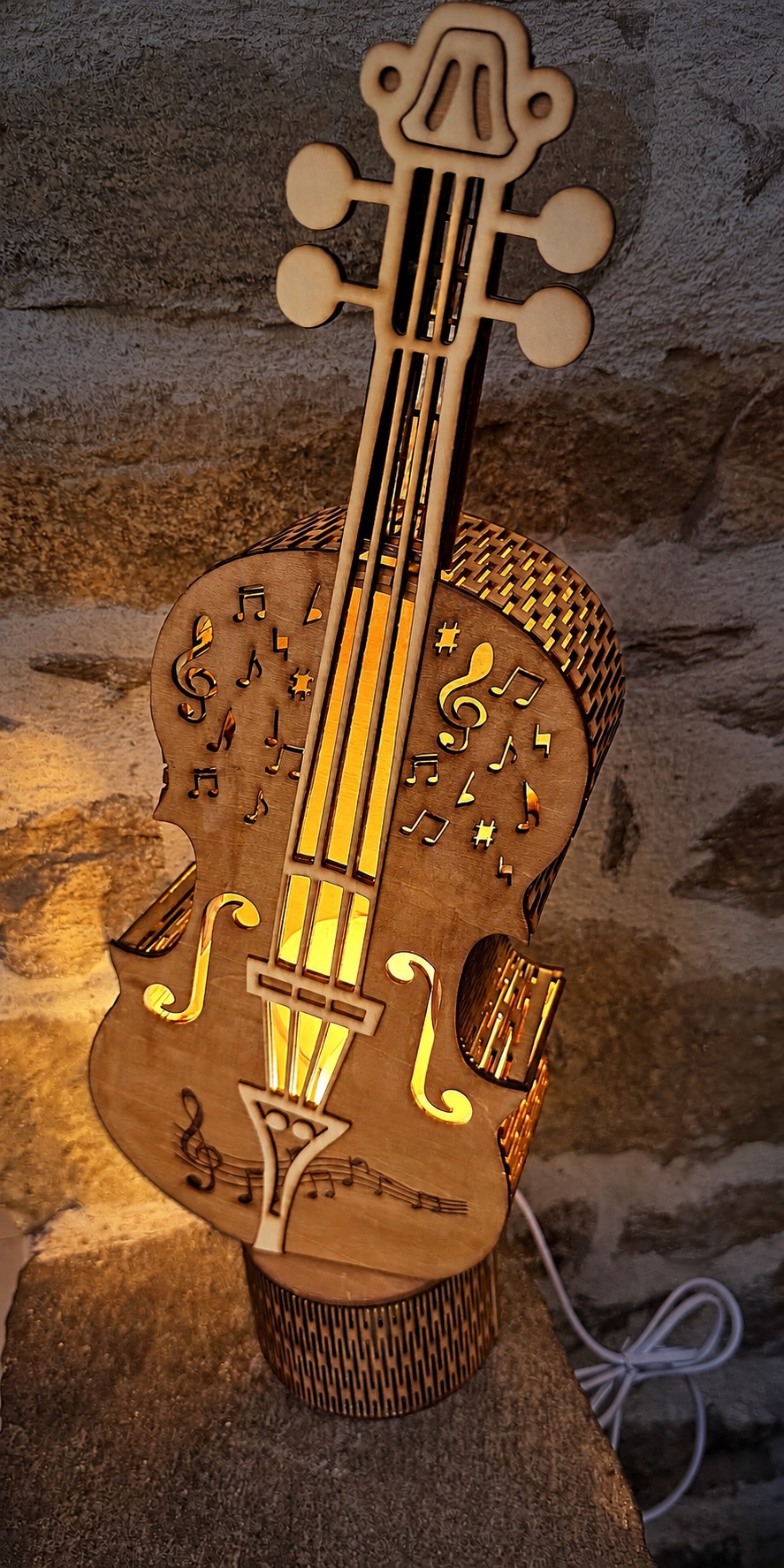 Reference LA 1b — illuminated wooden violin lamp against its darkened stone wall